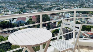 A balcony with a white table and chairs overlooking a cityscape with buildings and a pagoda. - Muong Thanh Grand Gia Lai (Pleiku)