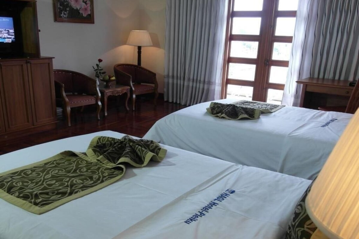 Une chambre d’hôtel avec deux lits, une télévision, un bureau, une chaise et une fenêtre avec des rideaux.