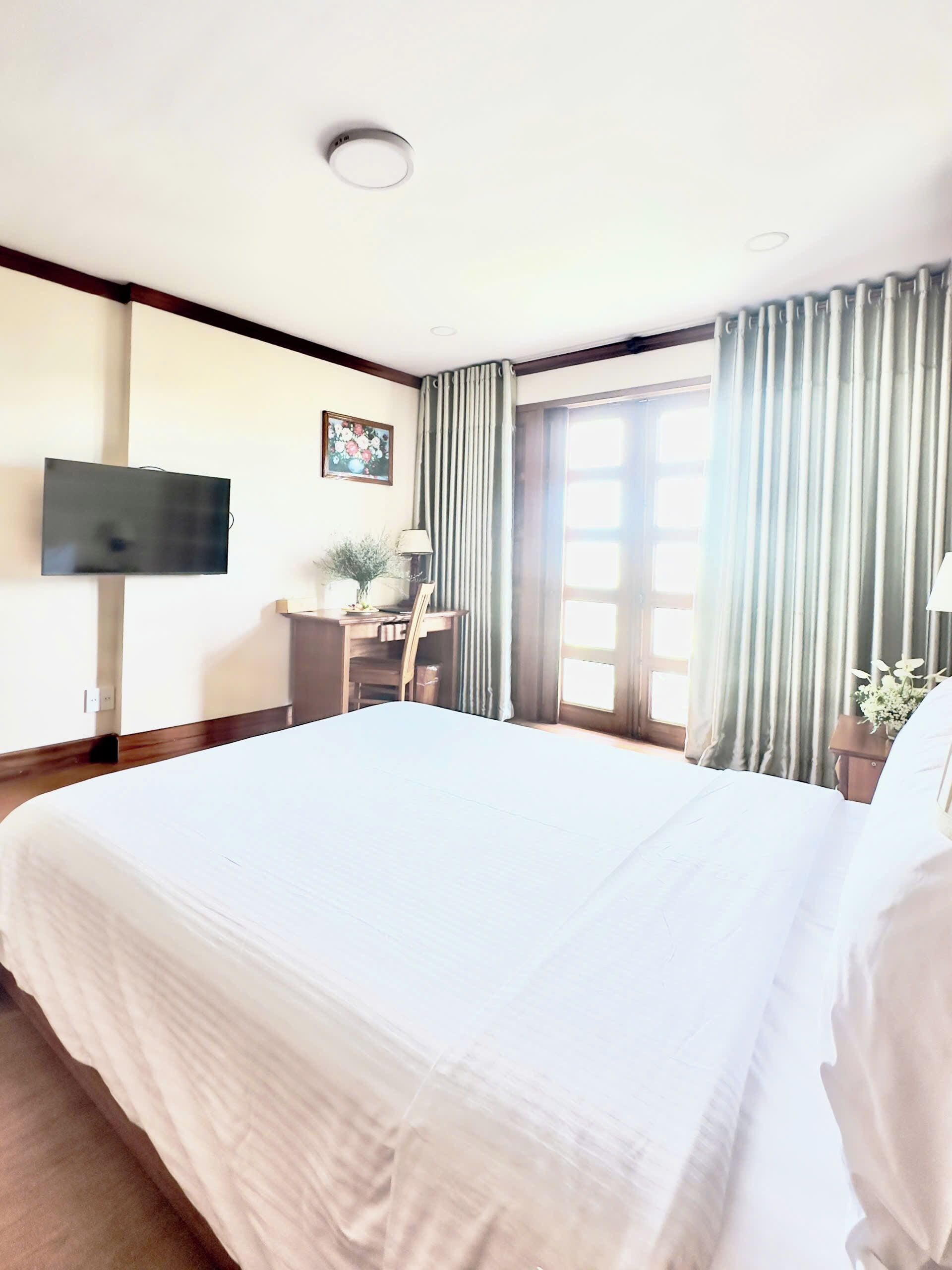 Une chambre d’hôtel avec un grand lit, un bureau avec une chaise, un téléviseur fixé au mur et une fenêtre avec des rideaux.