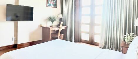 Une chambre d’hôtel avec un grand lit, un bureau avec une chaise, un téléviseur fixé au mur et une fenêtre avec des rideaux.