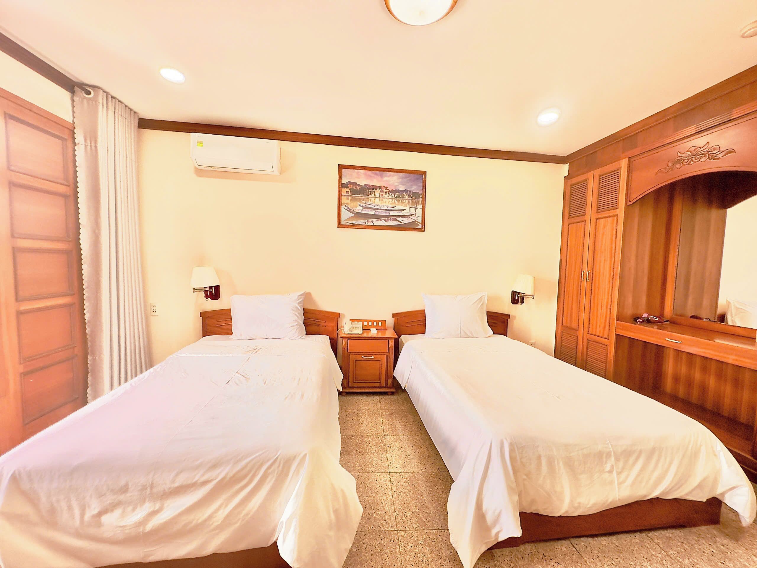 Una habitación de hotel con dos camas individuales, un armario de madera, un cuadro en la pared y una ventana con cortinas.