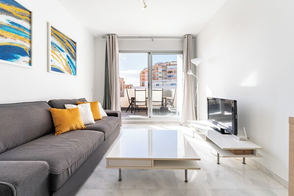 A modern living room with a grey sofa, a flat-screen TV, and a glass coffee table. - Cala Lucia I (Mijas)