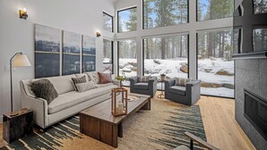 A spacious living room with a large window overlooking a snowy landscape, a fireplace, and a modern sofa set.