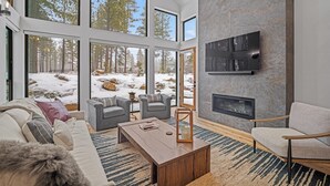 A modern living room with large windows, a fireplace, and a cozy seating area.