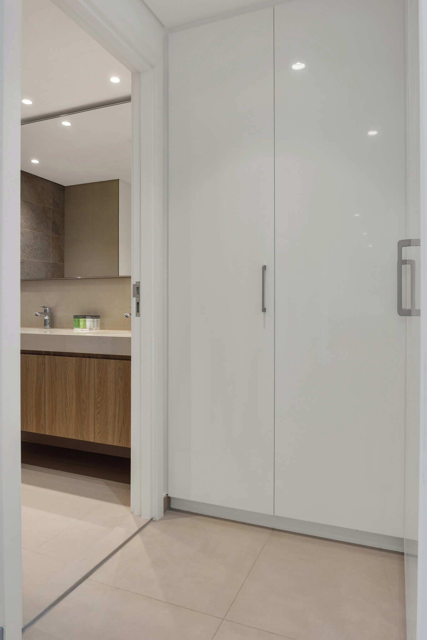 A modern bathroom with a white vanity, a wooden cabinet below, and a large white wardrobe with a handle.