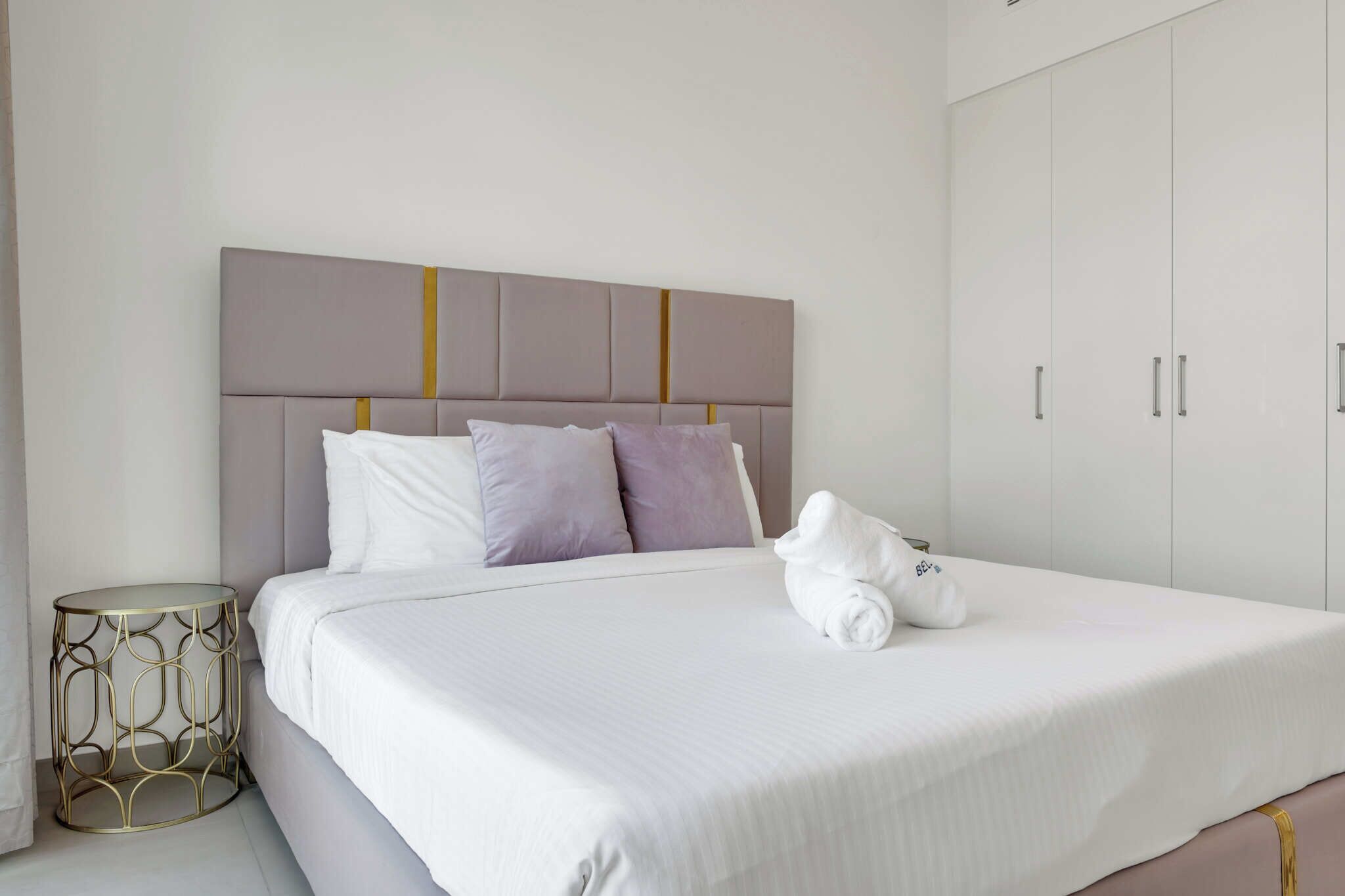 A neatly made bed with a headboard, pillows, and a rolled towel on the bed.