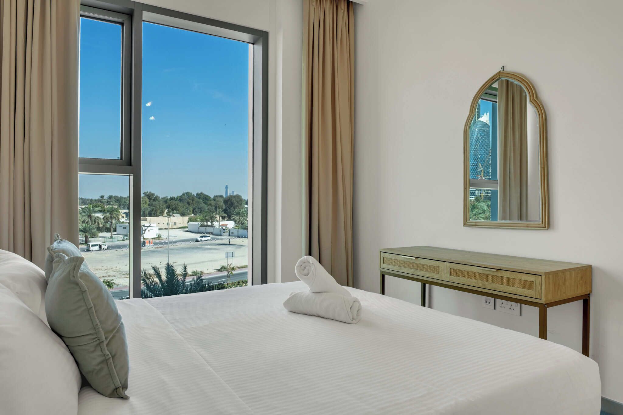 Una habitación de hotel con un ventanal grande, una cama, una mesita de noche y un espejo.