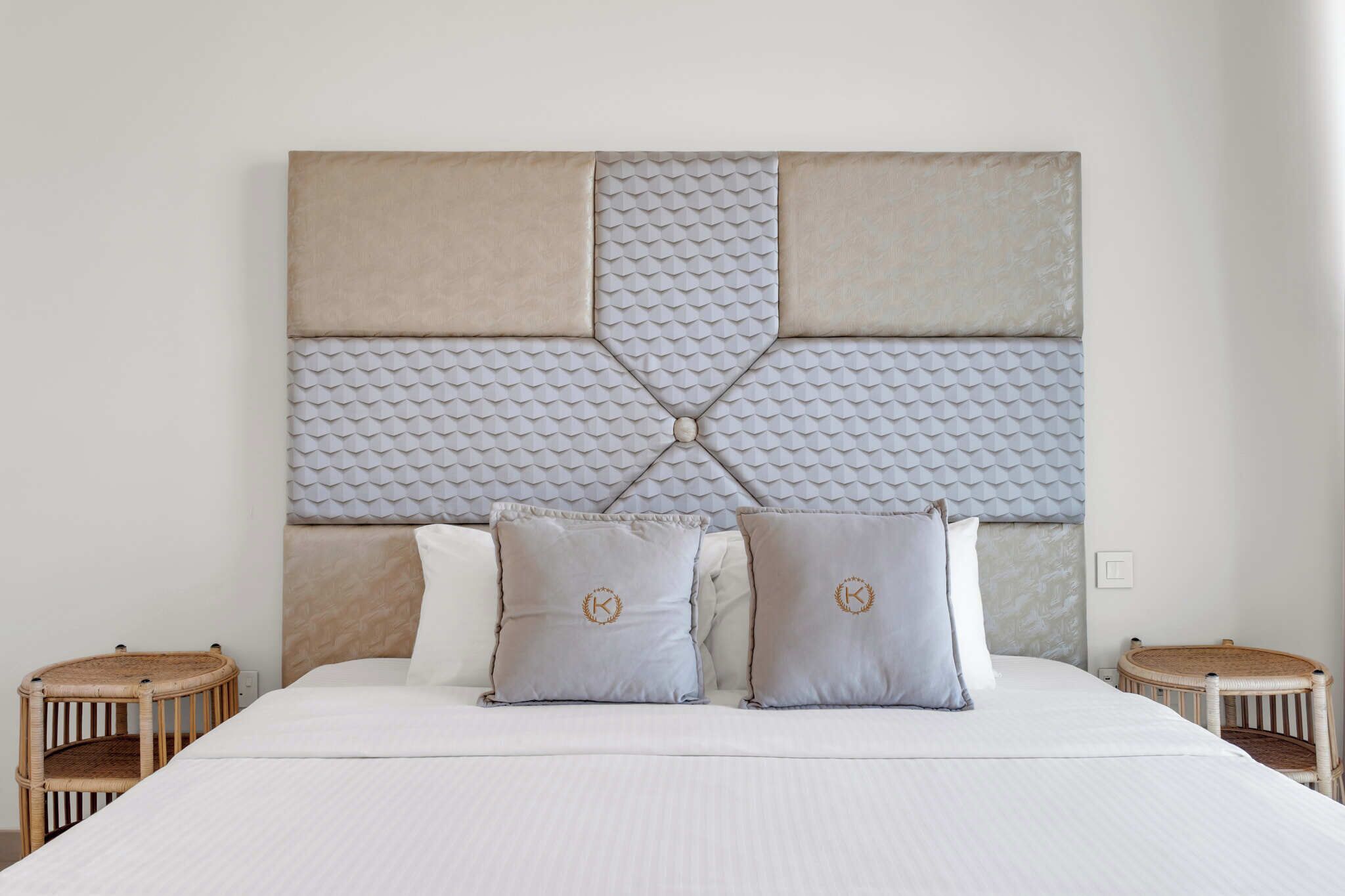 A neatly made bed with a large, textured headboard and two pillows with a monogram.