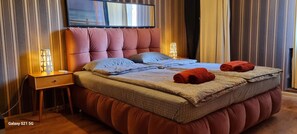 Ein modernes Schlafzimmer mit einer gepolsterten Kopfteil, einem flachbildfernseher über dem Bett und zwei Nachttischlampen.