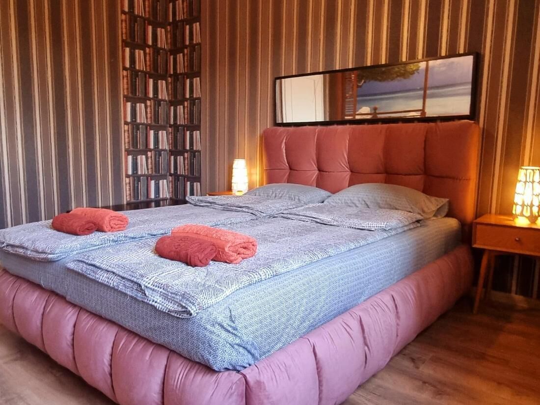A bedroom with a large bed, striped wallpaper, a bookshelf, and a painting on the wall.