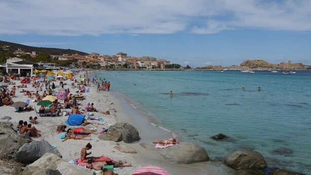 A crowded beach with people sunbathing and swimming, large rocks, and a clear view of the sea. - Apartment 500 m from seafront and center of Ile Rousse (L'Île-Rousse)