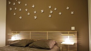 A bedroom with a bed, two bedside tables, and a wall with paper flowers. - Apartment 500 m from seafront and center of Ile Rousse (L'Île-Rousse)