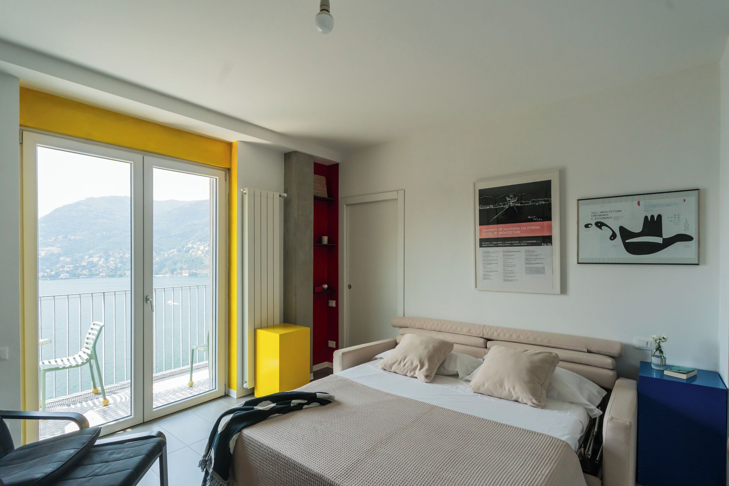 Une chambre à coucher avec un lit, une chaise, un balcon donnant sur la mer et une armoire rouge.