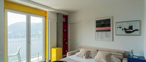 A bedroom with a bed, a chair, a balcony with a view of the sea, and a red wardrobe.