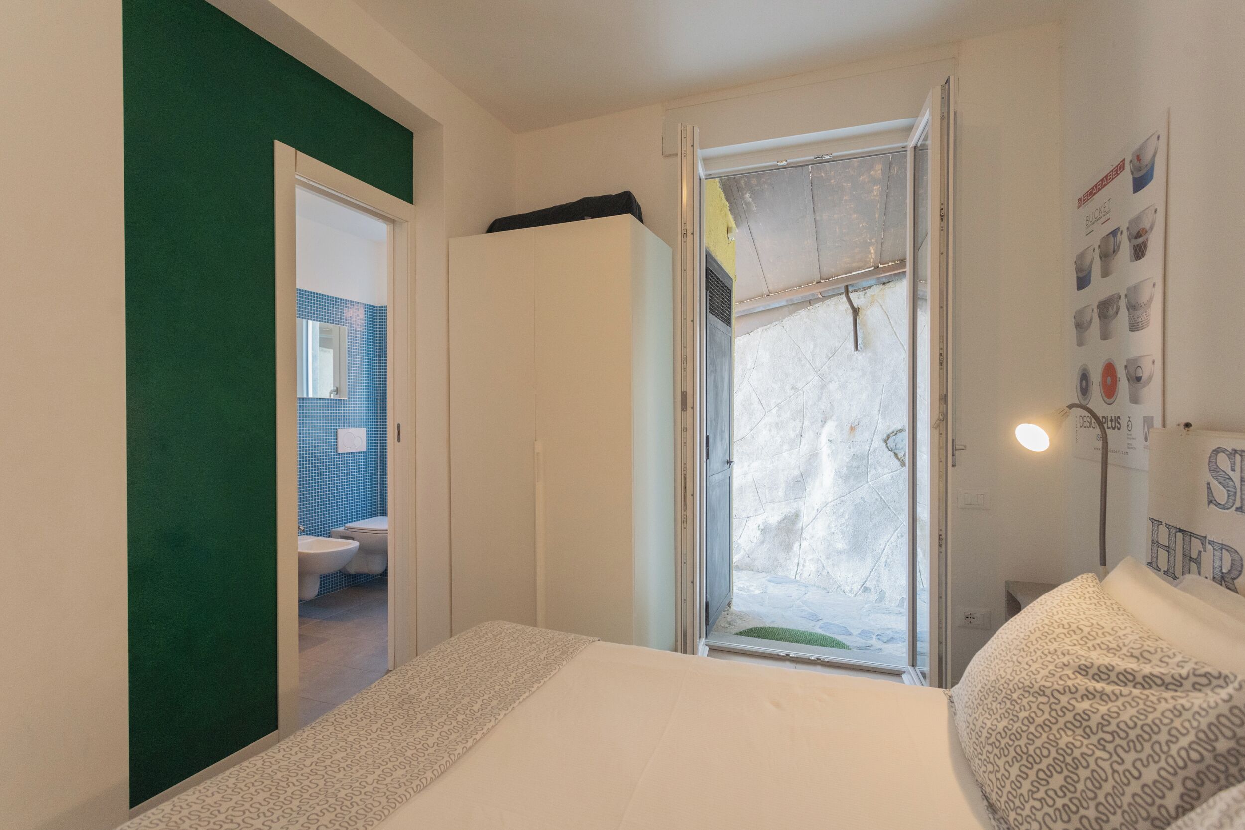 Un dormitorio con cama, ventana, puerta que da a un baño y una pared con un cartel.