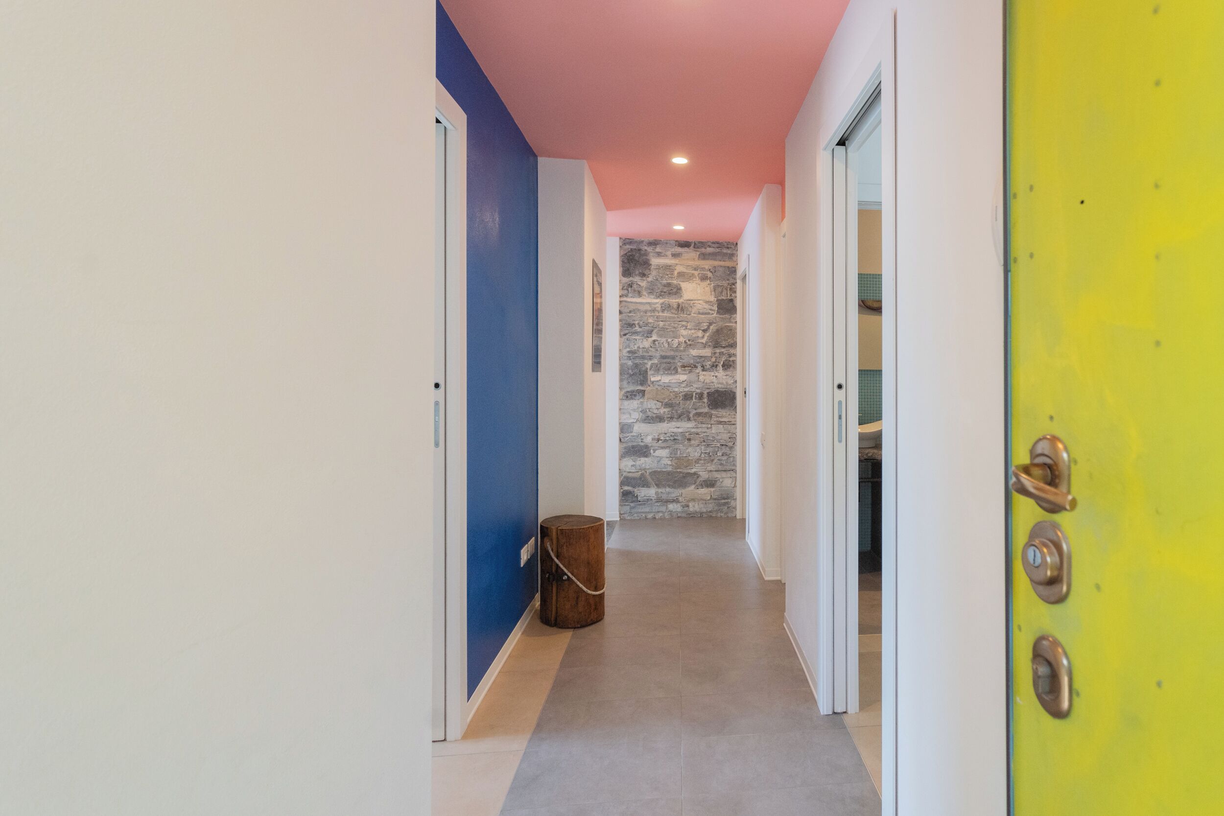 A hallway with a stone wall, a wooden stool, and a yellow door with a lock.