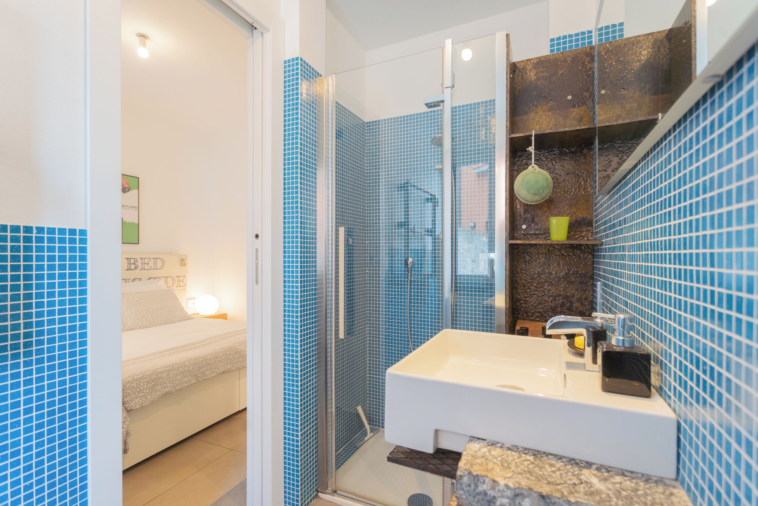 Un baño con cabina de ducha de vidrio, lavabo blanco y paredes con azulejos azules.