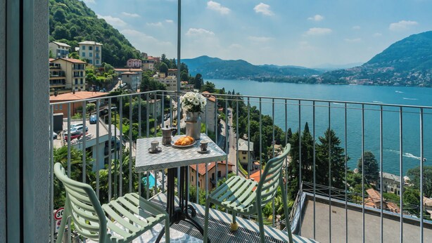 Ein Balkon mit Tisch für zwei Personen, mit Blick auf einen See und eine Berglandschaft.