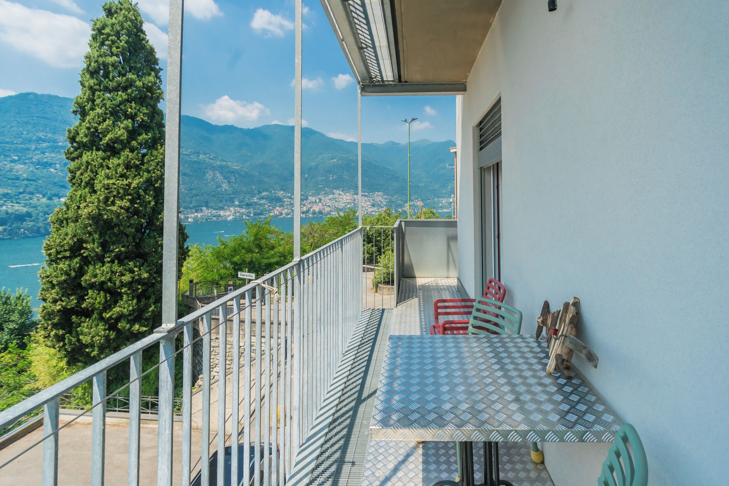A balcony with a table and chairs, overlooking a mountainous landscape and a body of water.