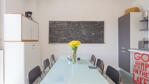 Ein Essbereich mit einem Glastisch, Stühlen, einer Vase mit gelben Blumen und einer Tafel mit Schrift.