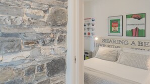 Ein Schlafzimmer mit einer Steinwand, einem Bett mit gemusterten Betttextilien und zwei gerahmten Postern an der Wand.