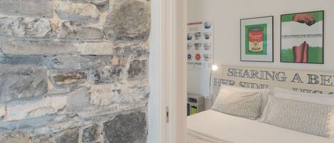 A bedroom with a stone wall, a bed with patterned bedding, and two framed posters on the wall.