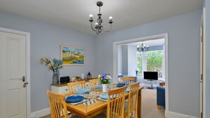 Een eetruimte met een houten tafel gedekt voor vier personen, een kroonluchter en een schilderij aan de muur.