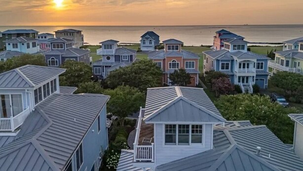 A coastal residential area with houses featuring gabled roofs and a view of the ocean at sunset. - Everyday Your Beachside Escape! (Cape Charles)