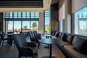A modern indoor seating area with tables and chairs, large windows, and a view of the cityscape.