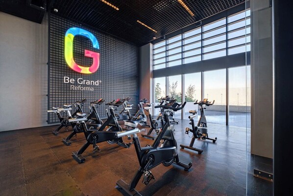 A gym with stationary bikes, a large logo on the wall, and large windows.