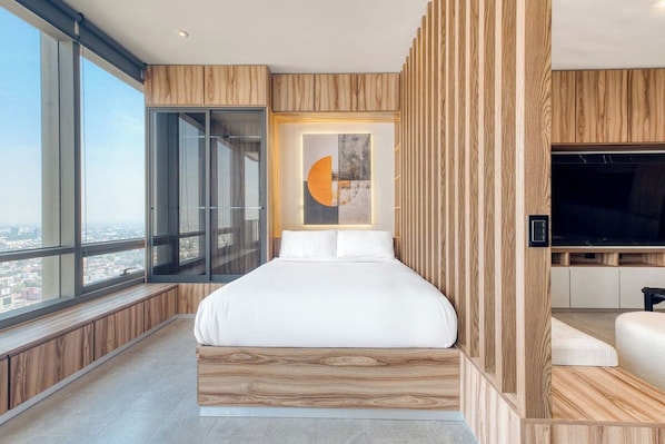 A modern bedroom with a large bed, a television, and a city view.