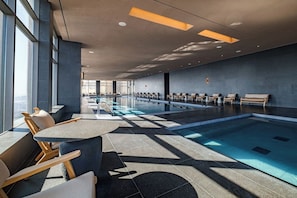 A modern indoor swimming pool with lounge chairs and a seating area.