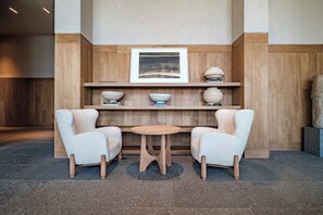 A lobby with a wooden reception desk, two upholstered chairs, a small round table, and a framed artwork above the desk. - Reforma Studio · Pool, Gym & Revolución Views (Ciudad de México)