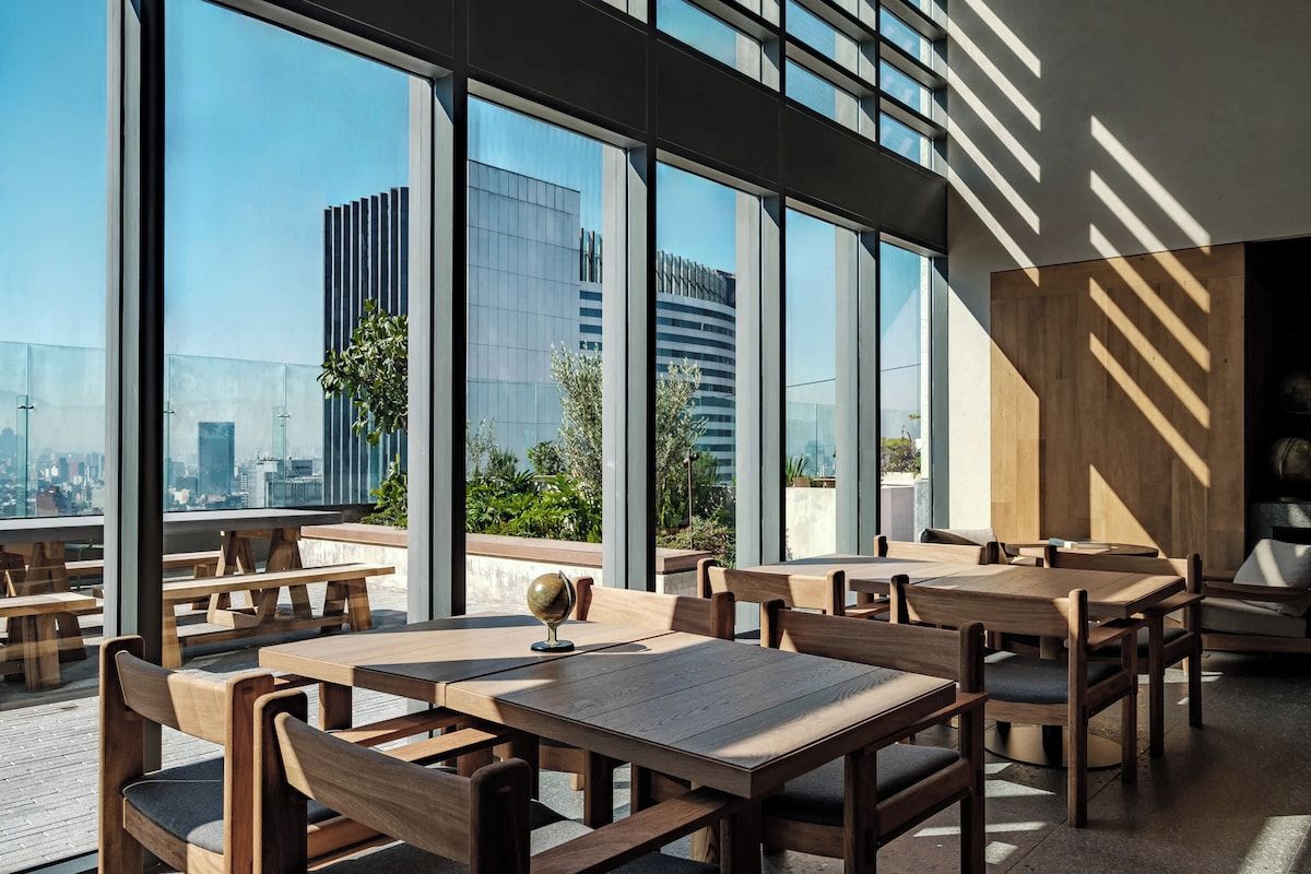 Un espace de restauration intérieur avec des tables et des chaises, de grandes fenêtres et une vue sur le paysage urbain.