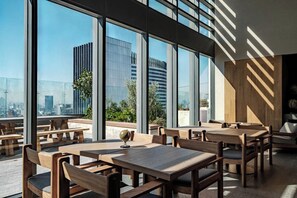 An indoor dining area with tables and chairs, large windows, and a view of the cityscape. - Reforma Studio · Pool, Gym & Revolución Views (Ciudad de México)