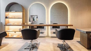 Een moderne kapsalon met een receptiebalie, twee zwarte kappersstoelen en een spiegel.