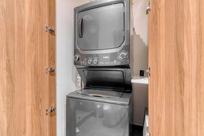 A compact washer and dryer unit installed in a wooden cabinet with metal hinges.