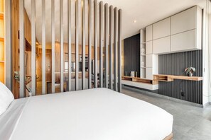 A modern bedroom with a large bed, a wooden partition, and a built-in desk with shelves.