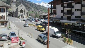 A street view with a church, parked cars, and a mountain in the background. - 50m from resort center, 4th floor, balcony, 24m², Le Grand Bornand (Le Grand-Bornand)