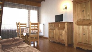 A cozy room with a wooden bed, a wooden dining table with chairs, a television on a wooden cabinet, and a large window with curtains. - 50m from resort center, 4th floor, balcony, 24m², Le Grand Bornand (Le Grand-Bornand)