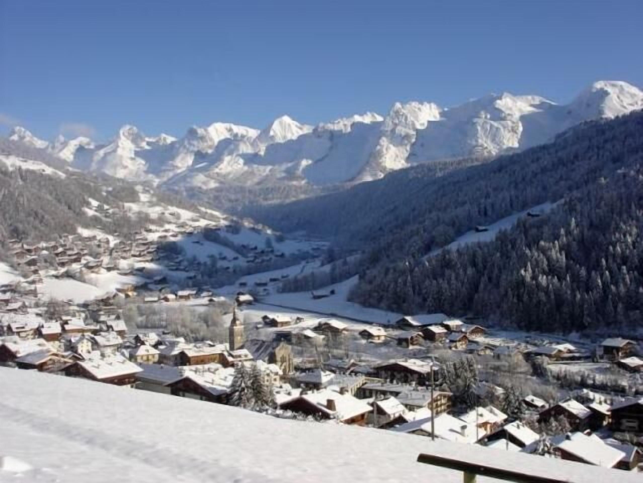 A snow-covered village with traditional wooden houses, a church, and a mountain backdrop.