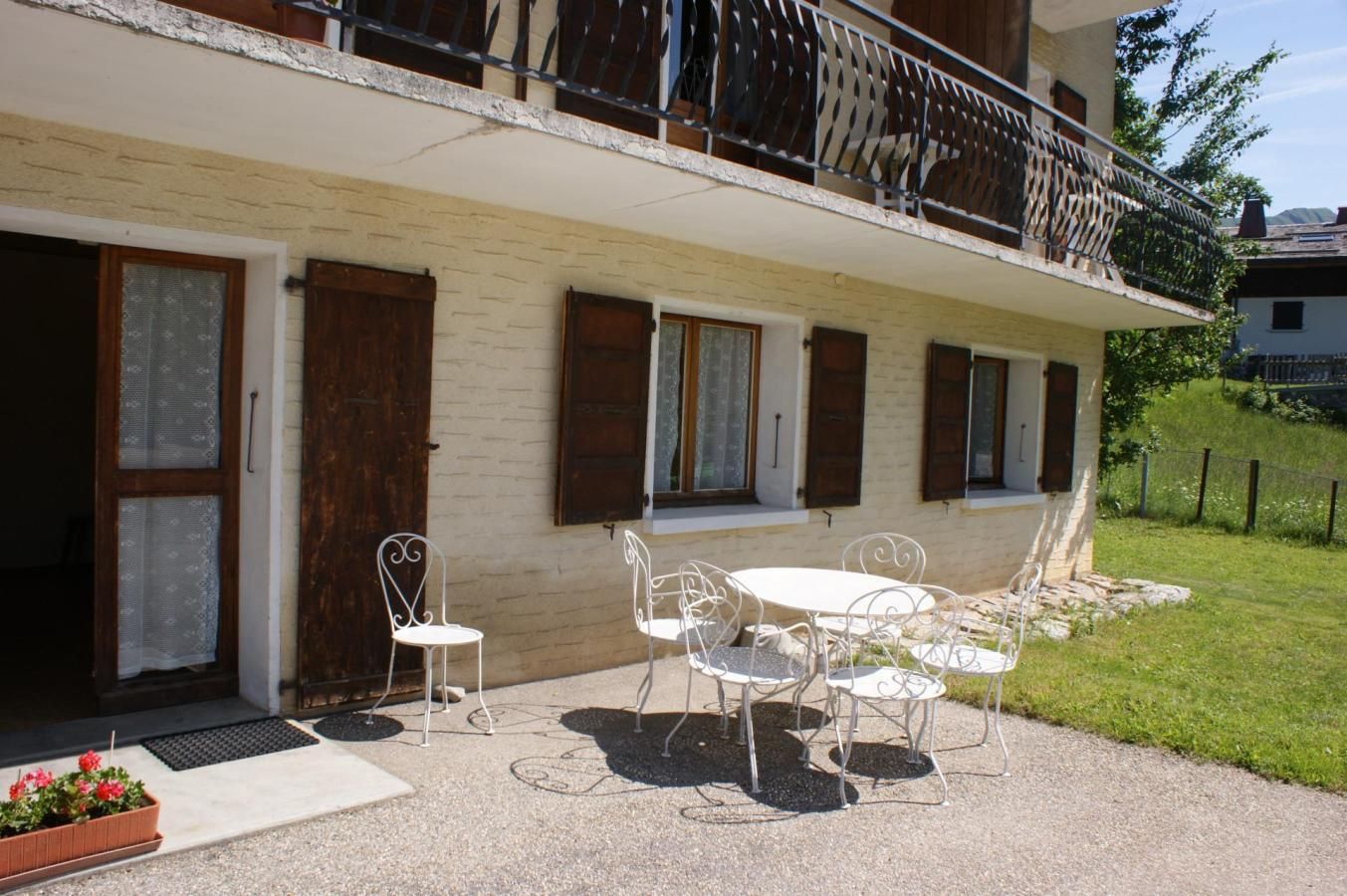 Un edificio con balcón, un patio con mobiliario exterior y un área con césped.