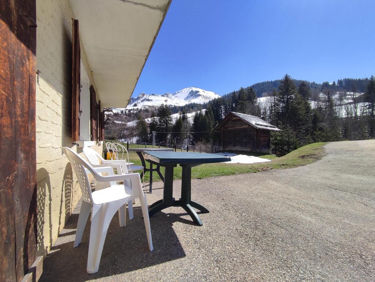 A patio with a table and chairs, a building with a sloped roof, and a mountain view.