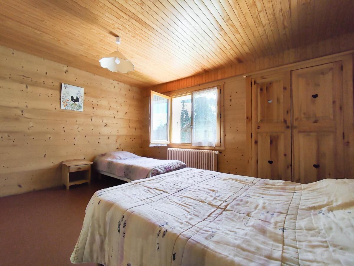 A wooden cabin room with a bed, a small table, and a window.