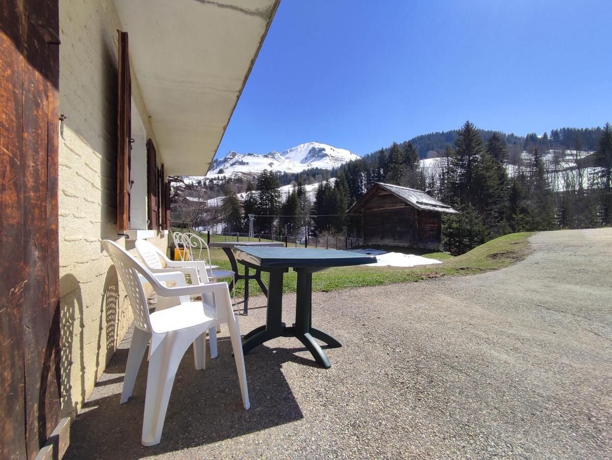 Eine Terrasse mit Tisch und Stühlen, ein Gebäude mit Satteldach und Blick auf die Berge.