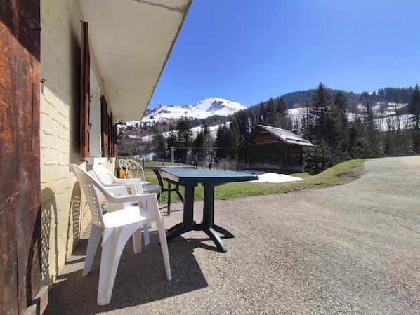 A patio with a table and chairs, a building with a sloped roof, and a mountain view.
