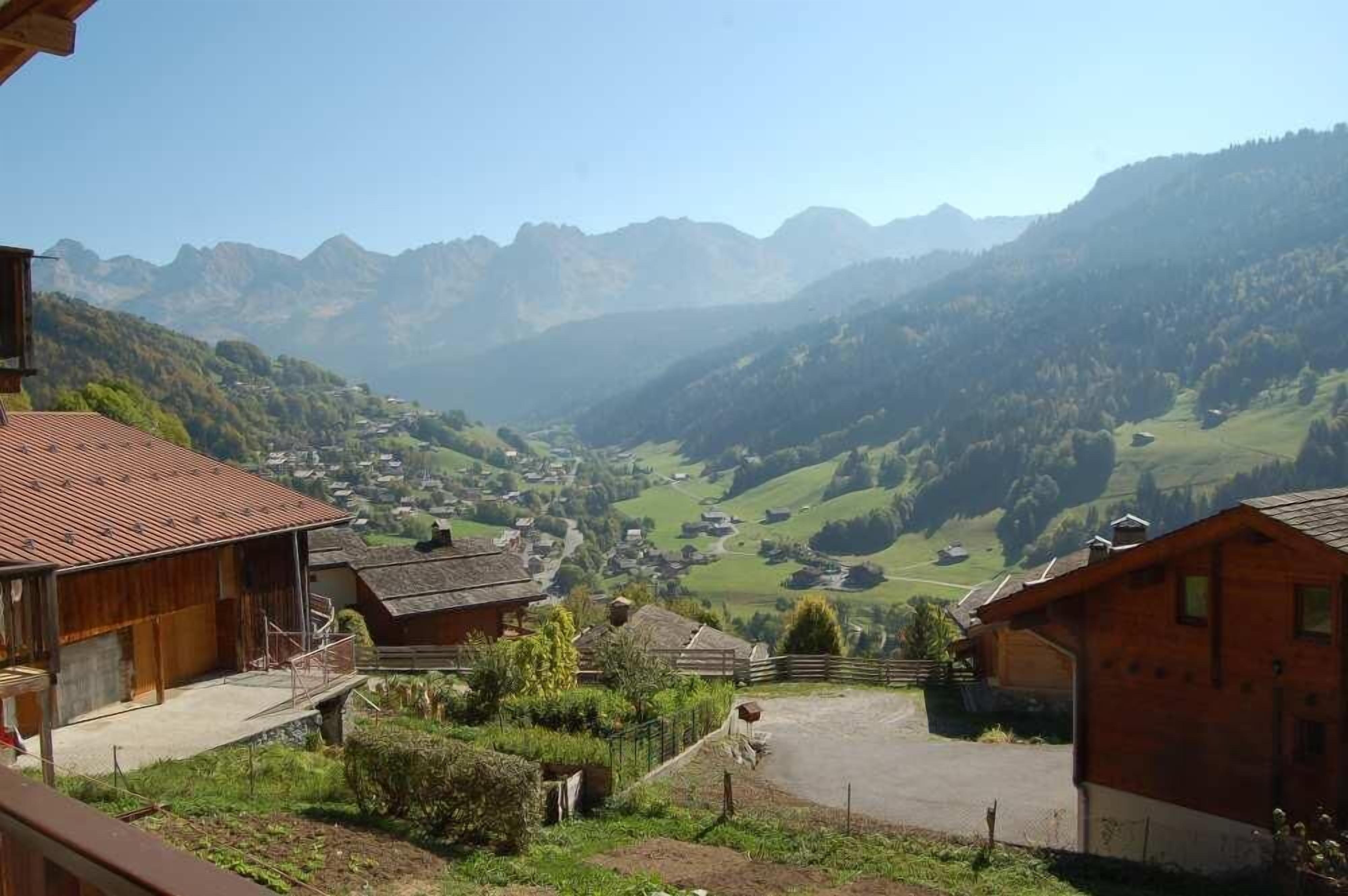 A rural village with traditional wooden houses, a clear view of the valley, and distant mountains.