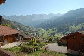 A rural village with traditional wooden houses, a clear view of the valley, and distant mountains.