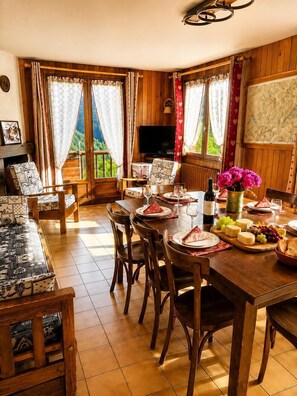 Un comedor con una mesa de madera dispuesta para una comida, sillas, un televisor y una vista panorámica a través de las ventanas.