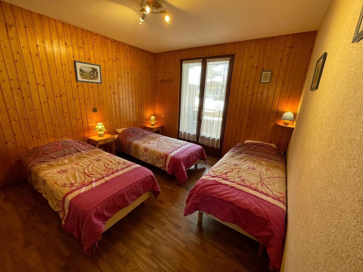 A room with wooden walls, two beds with pink bedding, a window with curtains, and a ceiling light.